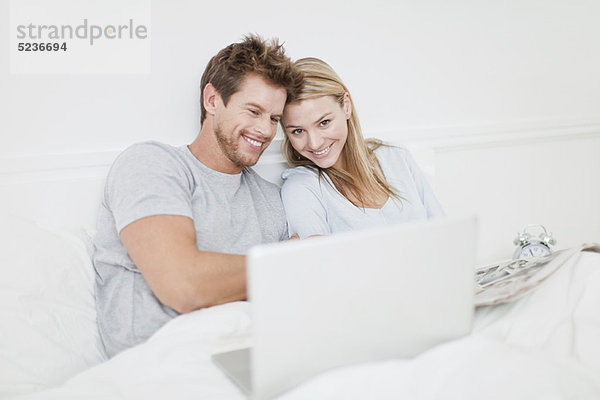 Lächelndes Paar mit Laptop im Bett