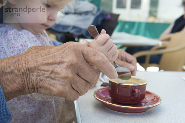 Kleinkind Mädchen hilft Großmutter rühren Tasse Kaffee  abgeschnitten