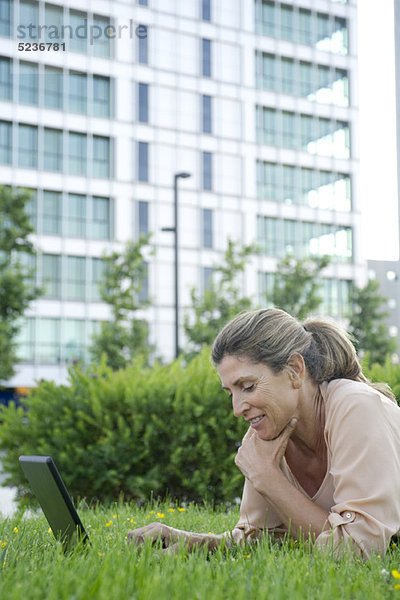 Frau im Gras liegend mit Laptop-Computer