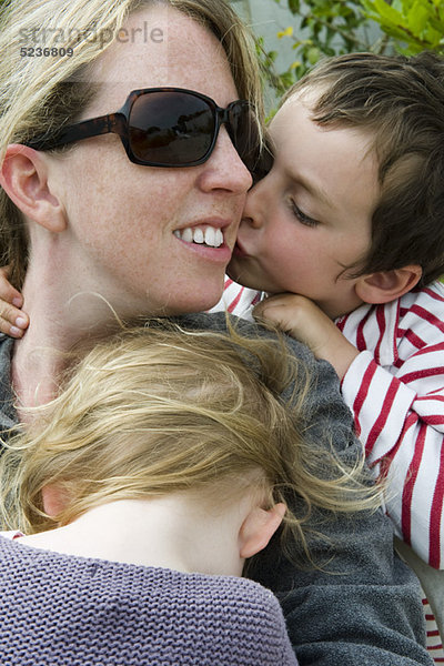 Mutter mit zwei kleinen Kindern  Sohn küsst ihre Wange