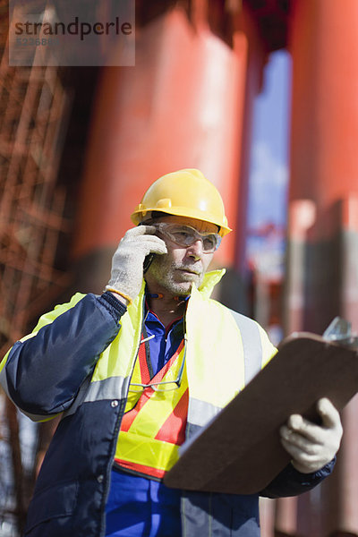 Arbeiter im Gespräch auf dem Handy auf der Bohrinsel