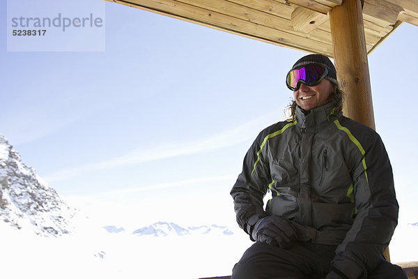 Mann entspannt auf dem Balkon der Skihütte