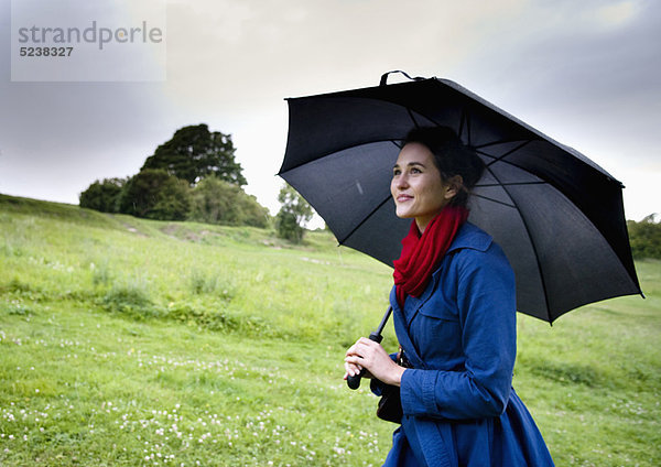 Frau hält Regenschirm im Feld