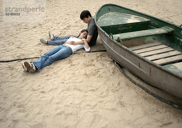 Paar  liegen neben altem Ruderboot im Sand