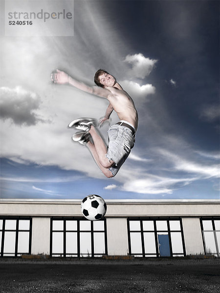 Junger Mann spielt auf Garagenplatz Fußball  Luftsprung