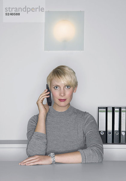 Frau sitzt an Tisch  telefoniert mit Handy