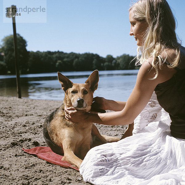 Frau sitzt mit Hund an Seeufer