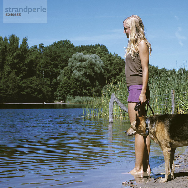 Frau steht mit Hund an Seeufer