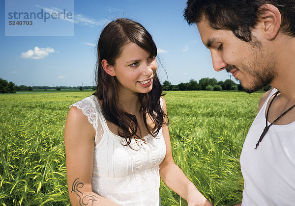 Junges Paar steht in Getreidefeld  er ist verlegen