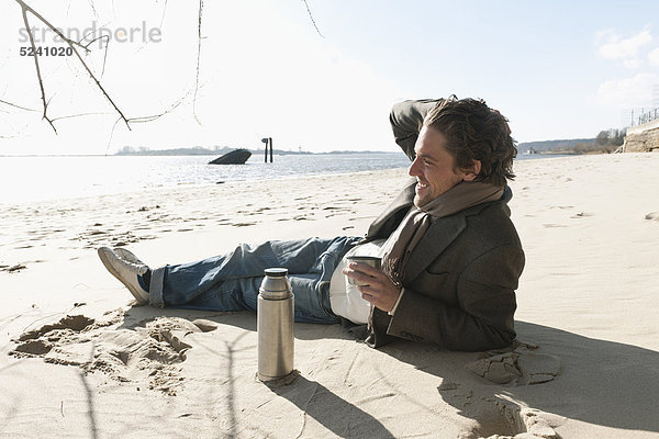 Auf Sand liegender Mann mit Kaffeekanne an der Elbe