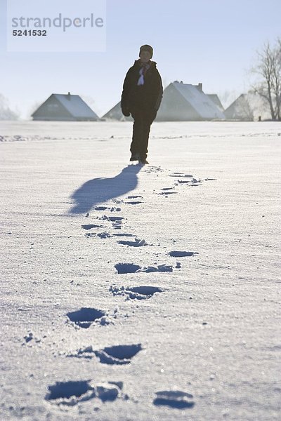 Junge läuft im Schnee mit Fußspuren im Vordergrund