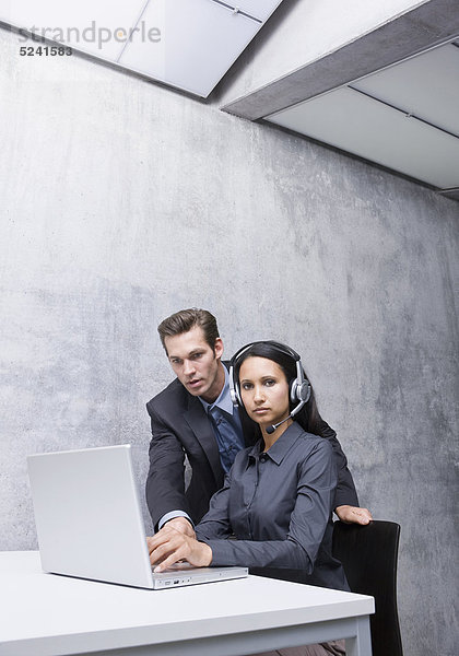 Frau und Mann in Büro an Laptop  sie mit Headset