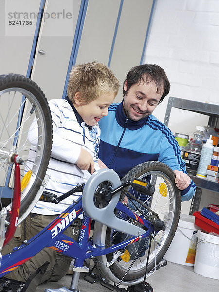 Vater und Sohn reparieren Fahrrad  Junge schraubt Rad fest