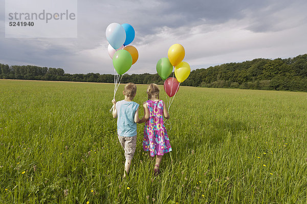 Deutschland  Nordrhein-Westfalen  Hennef  Mädchen und Junge halten Ballons und wandern auf der Wiese