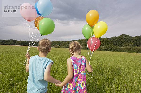 Deutschland  Nordrhein-Westfalen  Hennef  Mädchen und Junge halten Ballons und wandern auf der Wiese