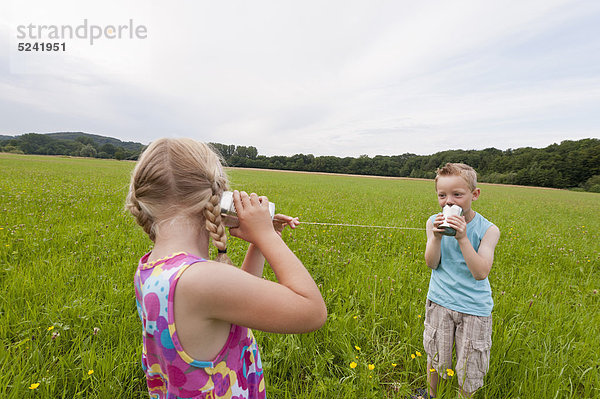 Deutschland  Nordrhein-Westfalen  Hennef  Junge und Mädchen auf der Wiese spielen mit Blechdose telefonieren