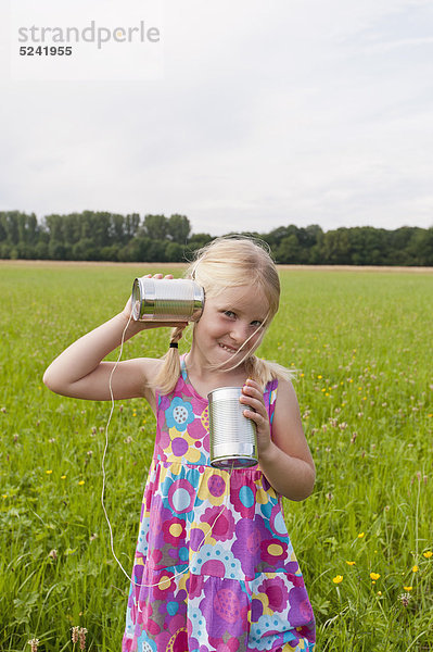 Deutschland  Nordrhein-Westfalen  Hennef  Mädchen stehen auf der Wiese und spielen mit Blechdose telefonieren