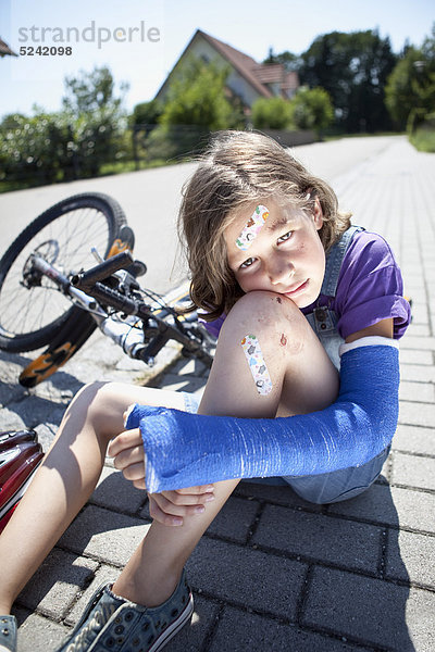 Verwundetes Mädchen sitzt nach Fahrradunfall auf der Straße
