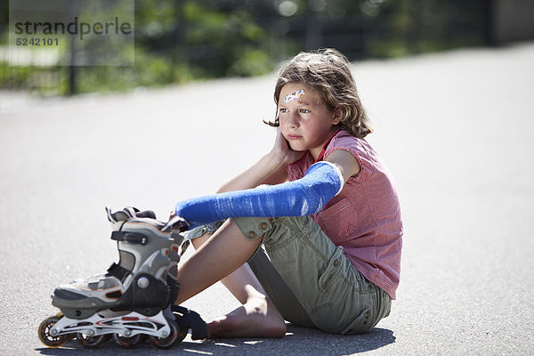 Verwundetes Mädchen nach Inline-Skate-Unfall auf der Straße sitzend