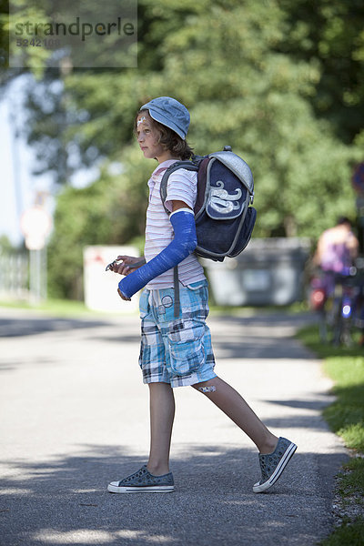 Verwundetes Mädchen mit Arm in Gips auf dem Weg zur Schule