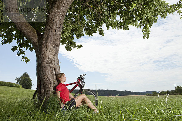 Junge Frau am Baum sitzend mit Mountainbike