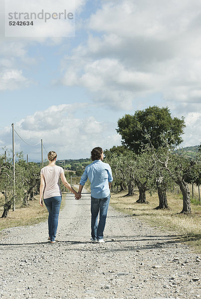 Italien  Toskana  Junges Paar hält Händchen und geht auf Landstraße