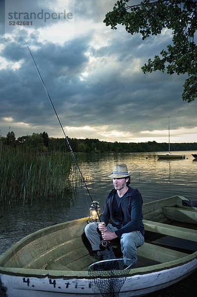 Mann mit Laterne beim Fischen im Boot in der Abenddämmerung