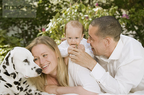Deutschland  Bayern  Vater  Mutter und Tochter mit Dalmatiner im Garten  lächelnd