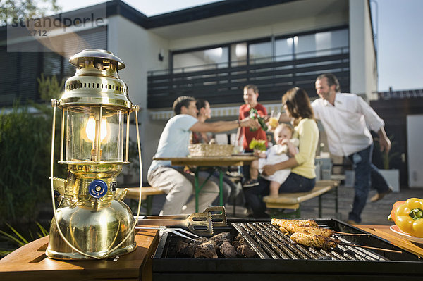 Deutschland  Bayern  Freunde beim Essen und Trinken mit Barbecue im Vordergrund