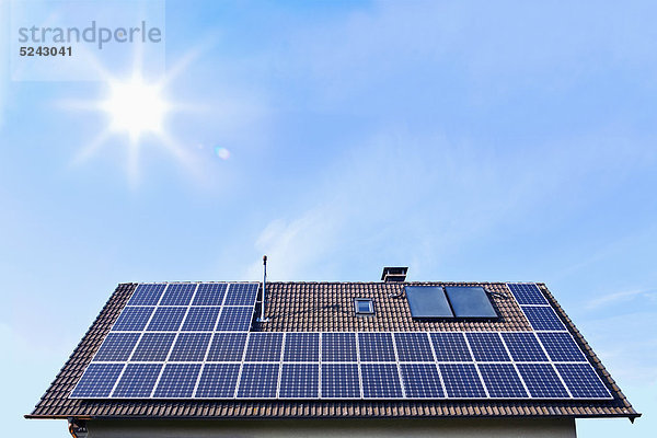 Deutschland  Solarmodule auf Hausdach vor blauem Himmel mit Sonne