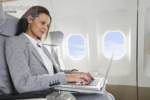 Mittlere erwachsene Geschäftsfrau mit Laptop in der Business Class Flugzeugkabine