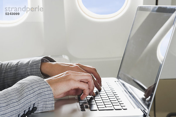Nahaufnahme der Hand der Geschäftsfrau mit Laptop in der Business Class Flugzeugkabine