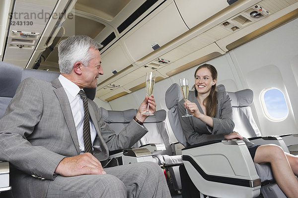 Geschäftsmann und Frau toasten Champagner in der Business Class Flugzeugkabine  lächelnd