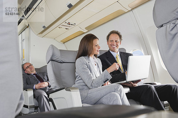 Geschäftsmann und Geschäftsfrau bei der Arbeit am Laptop in der Business Class Flugzeugkabine