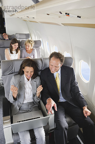 Deutschland  Bayern  München  Geschäftsleute am Laptop in der Business Class Flugzeugkabine  lächelnd