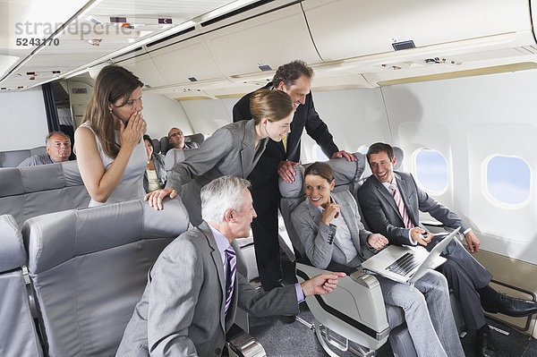 Deutschland  Bayern  München  Gruppe von Passagieren  die im Laptop in der Business Class Flugzeugkabine suchen  lächelnd