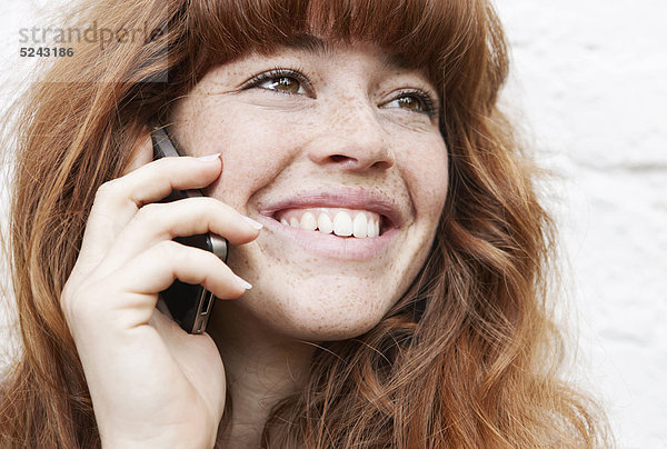 Nahaufnahme einer jungen Frau  die am Handy spricht und lächelt.