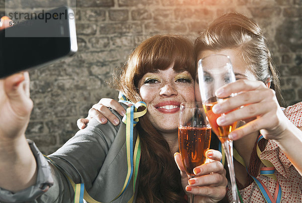 Nahaufnahme von jungen Frauen  die Champagnerglas halten und mit dem Handy fotografieren  lächelnd