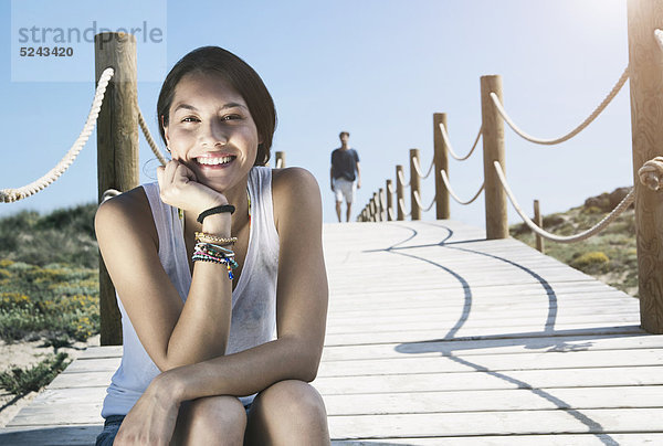 Spanien  Mallorca  Junge Frau auf Promenade sitzend und Mann im Hintergrund laufend