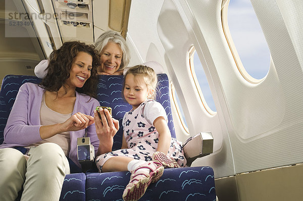 Frauen und Mädchen mit Handy neben dem Fenster im Economy-Class-Flugzeug