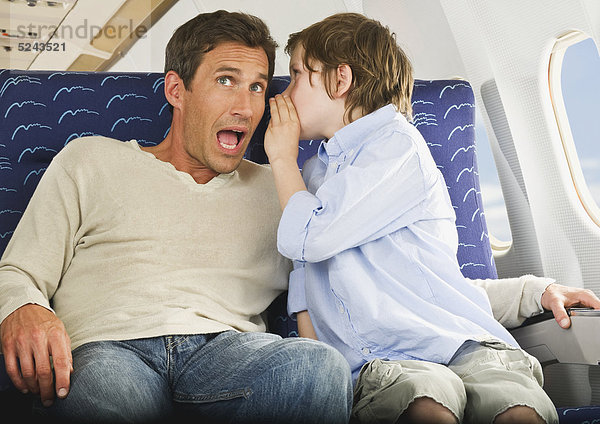 Junge flüstert dem Mann ins Ohr in einem Verkehrsflugzeug der Economy-Klasse.