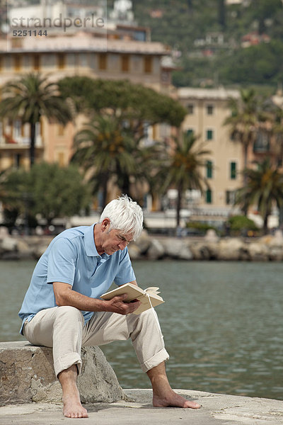 Senior sitzt mit Buch am Wasser  Italien  Rapallo