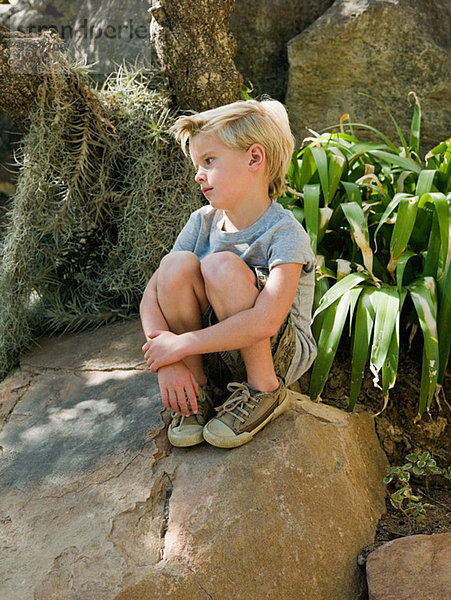 Nachdenklicher Junge auf dem Felsen sitzend