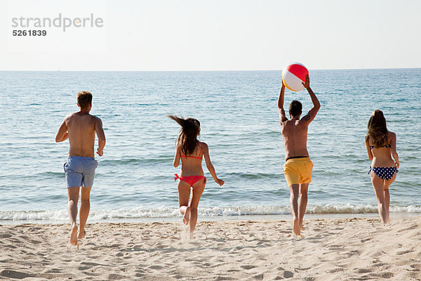 Vier Personen spielen mit Beachball am Strand