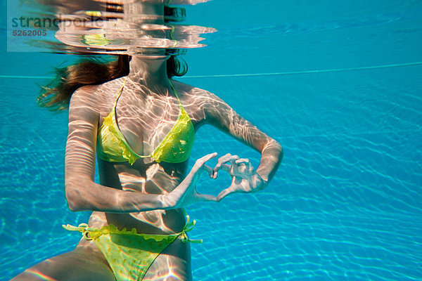 Junge Frau  die mit den Händen unter Wasser im Schwimmbad Herzform macht