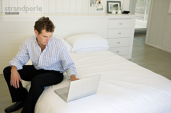 Mann sitzen auf dem Bett mit Laptop