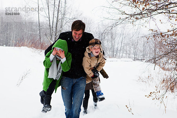 Vater trägt Sohn und Tochter im Schnee