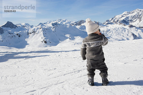 Kleiner Junge steht und schaut auf Berge im Schnee