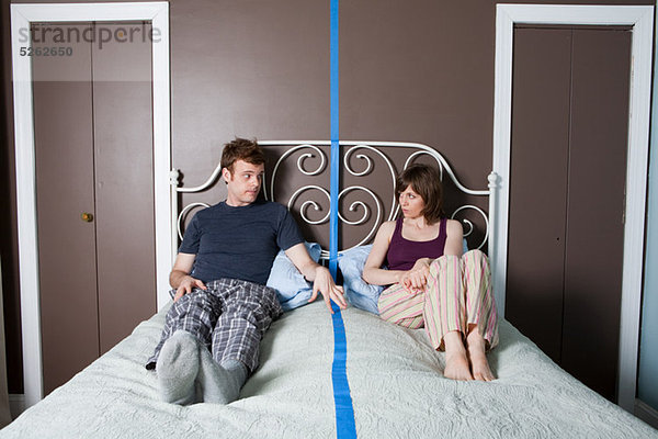 Junges Paar auf dem Bett sitzend  durch blaue Linie getrennt