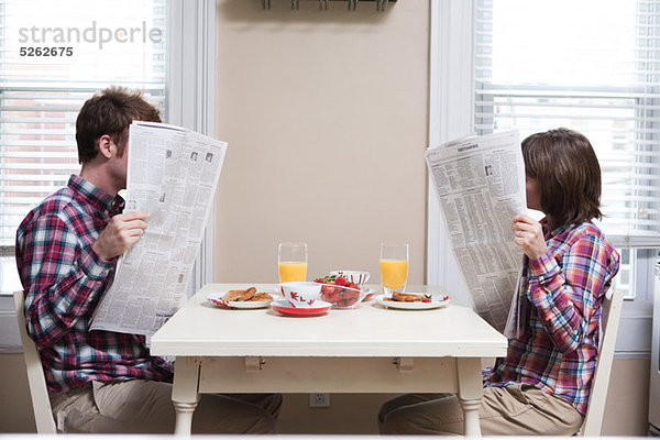 Junges Paar beim Zeitungslesen am Küchentisch